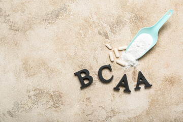 Letters BCAA, amino acid pills and powder on grunge background