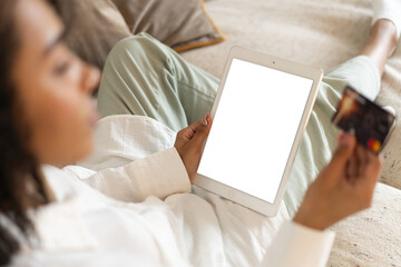 Young african american woman holding credit card and using tablet at home. Online shopping, e-commerce, internet banking. Transparent screen