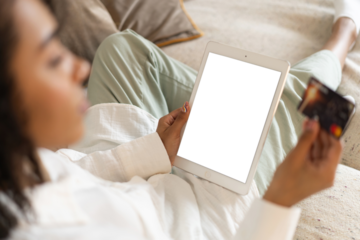 Young african american woman holding credit card and using tablet at home. Online shopping, e-commerce, internet banking. Transparent screen