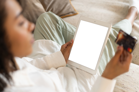 Young african american woman holding credit card and using tablet at home. Online shopping, e-commerce, internet banking. Transparent screen