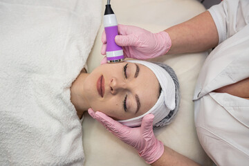 Obraz na płótnie Canvas Young woman applying apparatus phonophoresis procedure on face
