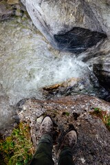 Vertical shot of someone's feet standing on a rock of waterfall