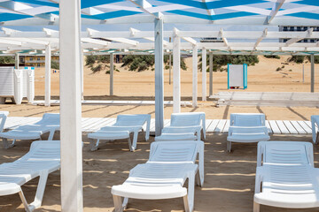 sandy beach on the sea coast with empty white sunbeds under a wooden canopy. Seaside resort
