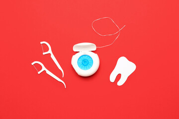 Dental floss, toothpicks and tooth model on red background