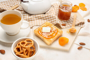 Tasty toast with apricot jam, cookies and cup of tea on light background