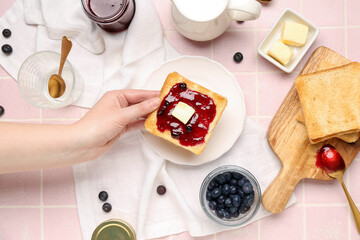 Woman holding tasty toast with blueberry jam on pink tile background