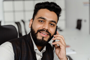 Young indian man in suit talking on cellphone while working at office