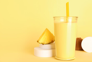 Glass of tasty pineapple smoothie, straw and coconut on yellow background