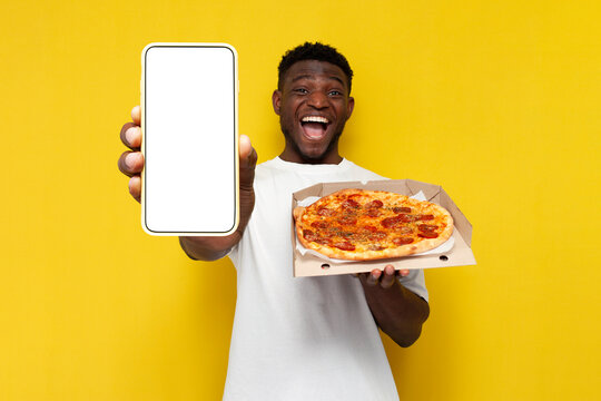happy african american man in white t-shirt holding pizza box and showing empty smartphone screen