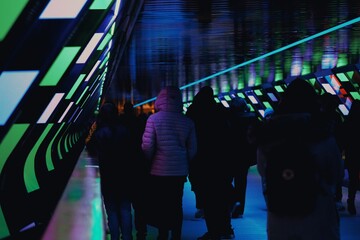 Crowd walking through an underground tunnel full of neon lights
