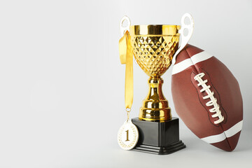 Gold cup with first place medal and rugby ball on light background