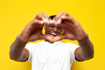 happy african american man in white t-shirt shows heart with his hands on yellow isolated background