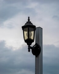 Fototapeta na wymiar Pole with lightbulb against dramatic gray sky, vertical shot