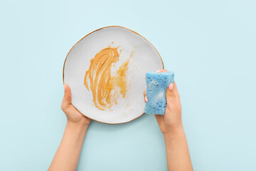 Female hands washing dirty plate with sponge on blue background