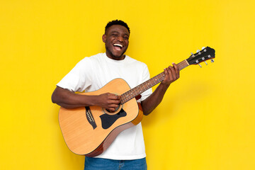 happy african american man holding guitar on yellow isolated background, musician guy in white...