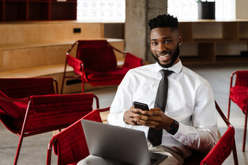 Young african american man using laptop and cellphone at office lobby
