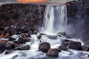 Scenic view of the Oxararfoss waterfall flowing over the rocks at sunset, Thingvellir