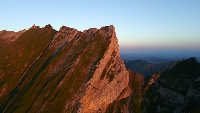 Drone footage of rocky Schafler mountain against pastel sunset sky in Switzerland