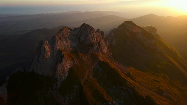 Drone footage of rocky Schafler mountain under bright sunlight during sunset in Switzerland