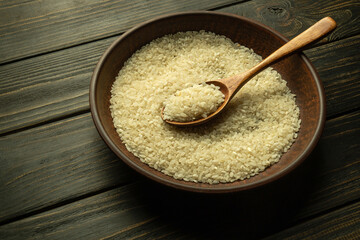 Vintage plate and spoon with raw rice groats before preparing the national dish on a dark kitchen table. Diet and healthy food with white rice