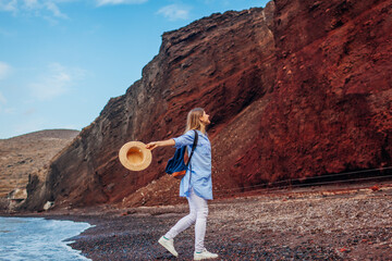 Traveler woman running along shore of Red beach on Santorini island, Greece feeling free and happy....