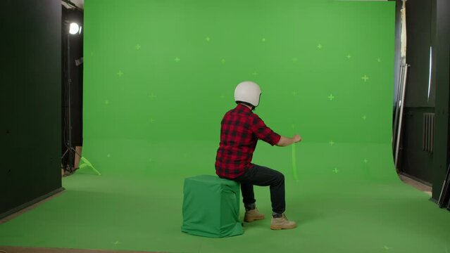 Man wearing a motorcycle helmet and pretending to drive a motorbike on a green background in the studio