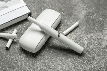 Modern electronic cigar and pack of sticks on grey grunge table