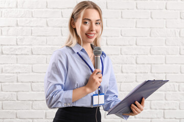 Female journalist with microphone and clipboard on white brick background