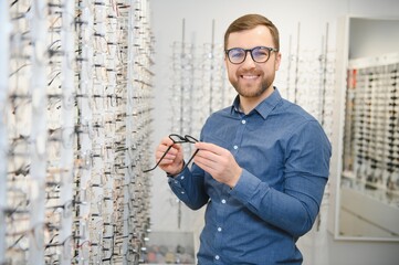 In Optics Shop. Portrait of male client holding and wearing different spectacles, choosing and...