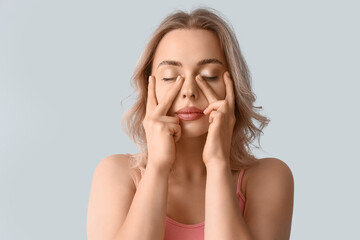 Young woman doing face building exercise on light background, closeup