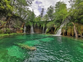 Waterfalls flowing into a clear lake surrounded by green trees at Plitvice Lakes National Park