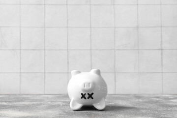 Piggy bank with closed eyes  on grunge table near white tile background. Concept of bankruptcy