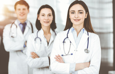 Group of young professional doctors standing as a team with arms crossed in sunny hospital. Medical help, insurance in health care, best disease treatment and medicine concept