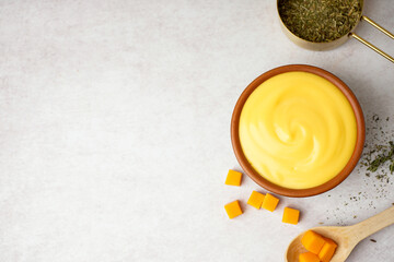 Bowl with tasty cheddar cheese sauce and measuring cup of rosemary on white grunge background