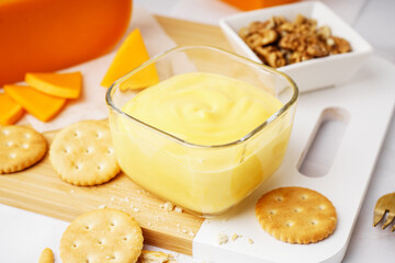 Bowls of tasty cheddar sauce with crackers, cheese chunks and walnuts on white grunge background
