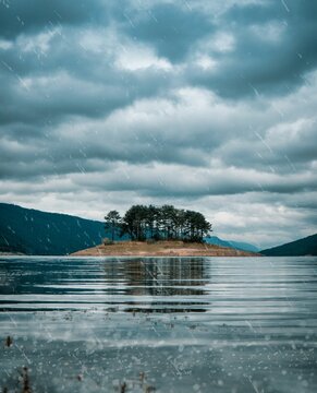 Vertical shot of a small island surrounded by a blue lake in cloudy sky background, Dospat, Bulgaria