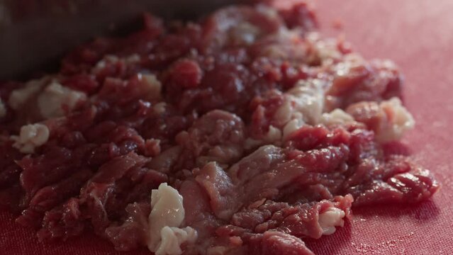 Mincing pork meat with big kitchen knife on cut board.