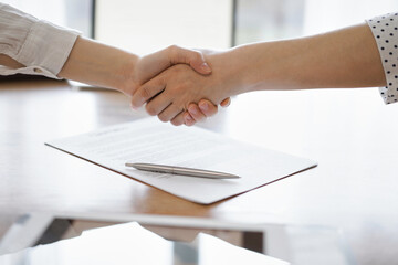 Fototapeta na wymiar Business people shaking hands above contract papers just signed on the wooden table, close up. Lawyers at meeting. Teamwork, partnership, success concept.