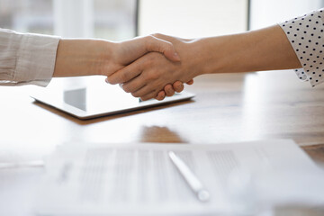 Fototapeta na wymiar Business people shaking hands above contract papers just signed on the wooden table, close up. Lawyers at work. Partnership, success concept.