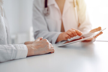 Doctor and patient sitting at the desk in clinic office. The focus is on female physician's hands...