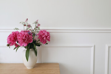 Beautiful floral bouquet. Vase with pink peonies flowers on ooden table, desk. White wall background with elegant moulding. Wedding or birthday concept. Elegant interior still life, web banner.