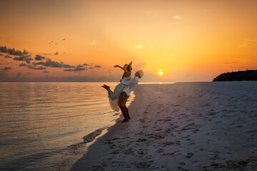 A happy couple on holidays hugging on a tropical beach in the Maldives during sunset time