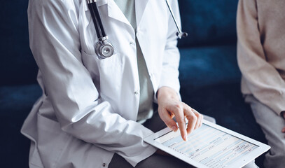 Doctor woman and kid boy patient at home. The pediatrician using tablet computer while filling up medical records, close up. Medicine, healthcare concept.