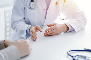 Doctor and patient discussing current health questions while sitting at the table in clinic office,...