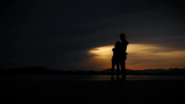 Resting mum and child silhouette by sea. A woman embrace her child silhouette on the bay against dark summer sky.