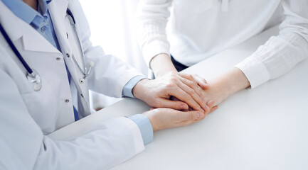 Doctor and patient sitting near each other at the table in clinic office. The focus is on female physician's hands reassuring woman, only hands, close up. Medicine concept. - 612556089