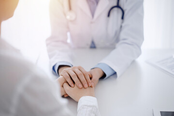Doctor and patient sitting opposite each other at the table in clinic office. The focus is on...