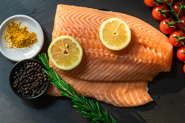 Top view of fresh raw salmon fish steak with spices on a dark stone background. Salt, spices, seasonings and other ingredients.