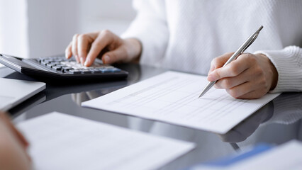 Woman accountant using a calculator and laptop computer while counting taxes for a client. Business audit concepts.