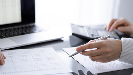 Woman accountant using a calculator and laptop computer while counting taxes for a client. Business...
